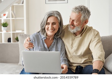 Happy mature mid age couple using laptop sit on sofa doing ecommerce shopping online on website. Smiling senior old adult man and woman looking at computer buying insurance browsing internet at home.