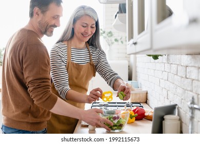 Happy mature middle-aged couple cooking vegetable vegetarian salad together in the kitchen, helping in preparation of food meal. Family moments, domestic homemade food - Powered by Shutterstock