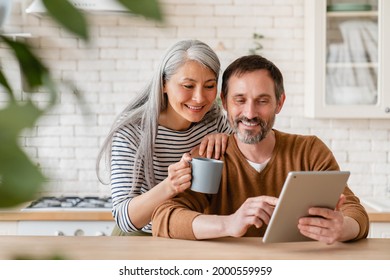 Happy mature middle-aged family couple parents husband and wife checking emails, reading news on digital tablet during breakfast, choosing new house, using application online - Powered by Shutterstock