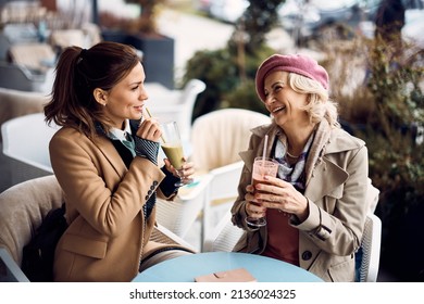 Happy Mature Mother Talking To Her Daughter While Drinking Smoothie In An Outdoor Cafe. 