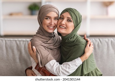 Happy Mature Muslim Mother And Adult Daughter Hugging Posing Wearing Hijab Sitting On Couch In Living Room At Home, Smiling To Camera. Middle-Eastern Family Happiness Concept - Powered by Shutterstock