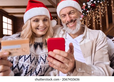 Happy mature old couple customers wear santa hats using cell phone hold credit card at home buy Christmas presents doing online ecommerce shopping purchase payment in mobile app on smartphone. - Powered by Shutterstock