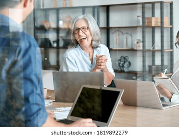 Happy mature old female mentor coach supervisor training young interns at group office meeting professional workshop. Cheerful middle aged teacher professor laughing with students at university class.