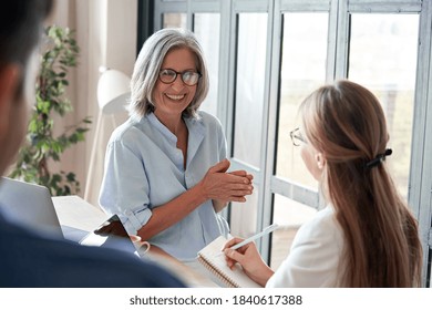 Happy mature old female mentor coach laughing training young interns at group office meeting professional workshop. Cheerful middle aged teacher professor talking to students at university seminar. - Powered by Shutterstock