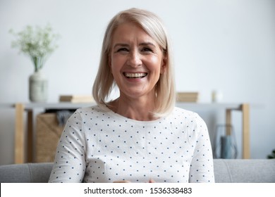Happy mature old woman blogger looking at camera at home, smiling middle aged senior lady sit on sofa talking by webcam laughing enjoying video conference call online or shooting blog vlog at home