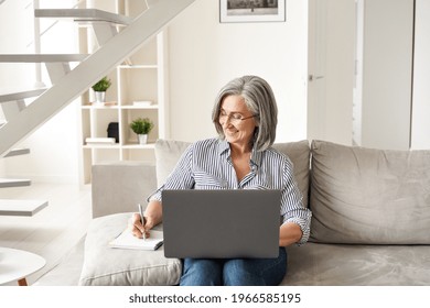 Happy Mature Old Woman Working On Laptop From Home Office. Smiling Senior Lady Watching Online Training Webinar Using Computer Remote Working Or E Learning Class, Having Virtual Meeting, Writing Notes