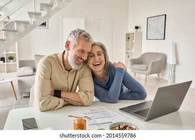 Happy mature older family couple laughing, bonding sitting at home table with laptop. Smiling middle aged senior 50s husband and wife having fun satisfied with buying insurance, paying bills online. - Shutterstock ID 2014559786