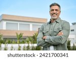 Happy mature older Latin man new property buyer modern villa owner or realtor salesman standing outside home, smiling middle aged homeowner posing outdoor near country house. Portrait.