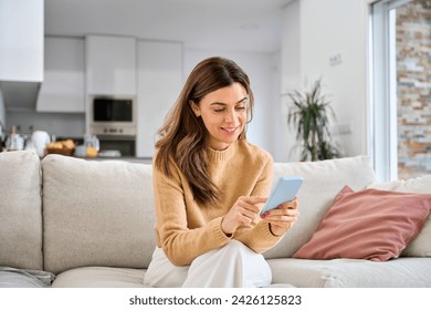 Happy mature older woman using smartphone sitting on couch at home. Smiling middle aged woman looking at cell phone messaging or doing ecommerce mobile shopping relaxing on sofa in living room. - Powered by Shutterstock