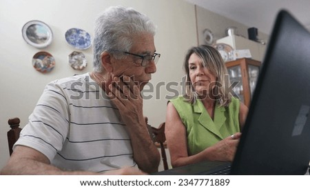 Happy mature people spontaneous laugh and smile in front of laptop computer, authentic real life joyful interaction between older couple bursts in laughter