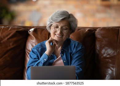 Happy Mature Retired Woman In Glasses Looking At Laptop Screen, Reading News Or Watching Tv Series Online. Smiling Middle Aged Granny Communicating In Social Network, Old People And Modern Tech.