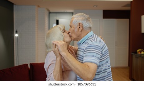 Happy Mature Senior Couple Dancing Laughing In Kitchen At Home. Beautiful Romantic Middle Aged Older Grandparents Relaxing, Making A Kiss, Celebrating Anniversary Together, Enjoy Care Love Tenderness