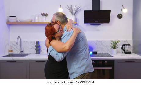 Happy Mature Senior Couple Dancing Laughing In The Kitchen, Beautiful Romantic Middle Aged Older Grandparents Relaxing Having Fun Together At Home Celebrating Anniversary Enjoy Care Love Tenderness.