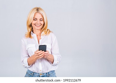 Happy mature senior woman holding smartphone using mobile online apps, smiling old middle aged lady texting sms message chatting on phone looking at cellphone isolated on white grey background - Powered by Shutterstock