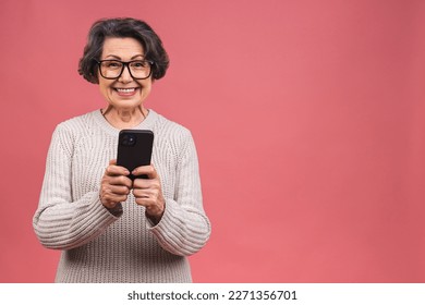 Happy mature senior woman holding smartphone using mobile online apps, smiling old middle aged grandmother texting sms message chatting on phone isolated over pink background. - Powered by Shutterstock