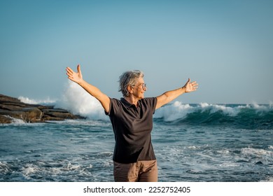 Happy mature senior woman with outstretched arms standing on the beach at sunset looking away enjoying vacation and freedom - Powered by Shutterstock