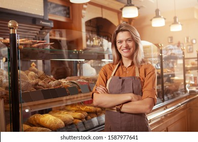 Happy mature small bakery owner smiling proudly at her confectionery store. Cheerful female baker working at her shop