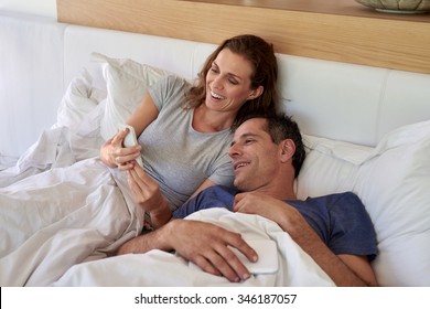 Happy mature smiling husband wife couple looking at mobile cell phone while laying in the bed - Powered by Shutterstock