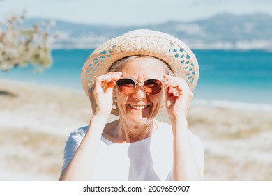 Happy Mature Woman Of 50 Years On The Beach With Trendy Sunglasses And A Hat,happy Smiling Senior Woman, Vacation And Summer Concept