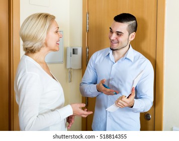 Happy Mature Woman Answers The Questions Of Adult Employee  In Door At Home. Focus On The Man