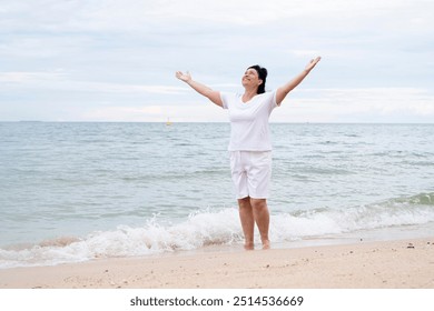 Happy mature woman with arms outstretched feeling the breeze at beach. Mid lady feeling good and enjoying freedom at sea, copy space - Powered by Shutterstock