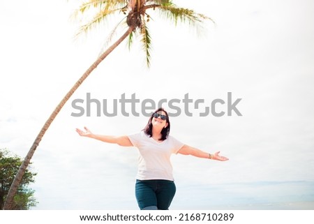 Happy mature woman with arms raised on the beach, enjoying life. Woman having fun and expressing joy and well being.
