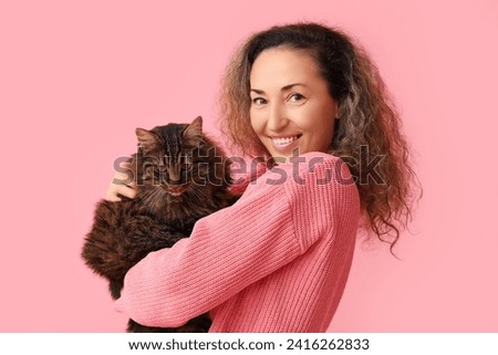 Happy mature woman with cute cat on pink background