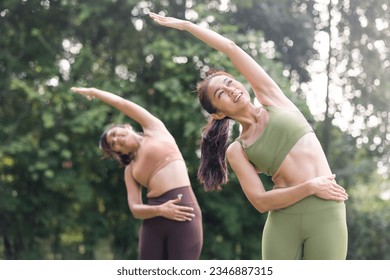 Happy mature woman doing yoga pose and stretching on nature background. Smiling Asian female practicing yoga outdoor with friends. Healthy lifestyle concept. - Powered by Shutterstock