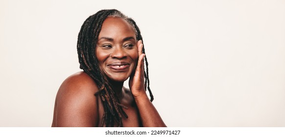 Happy mature woman with dreadlocks smiling while touching her flawless skin. Cheerful dark-skinned woman embracing her beautiful melanated skin. Mature black woman ageing gracefully.