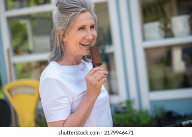 A Happy Mature Woman Eating Ice-cream And Looking Enjoyed