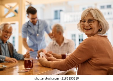 Happy mature woman enjoying in playing card with her friends on patio at residential care home. - Powered by Shutterstock