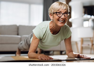 Happy mature woman exercising in plank position on a floor in the living room