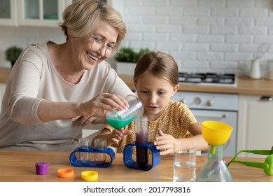 Happy mature woman in glasses with curious little girl making funny experiments in kitchen, smiling aged grandmother and adorable granddaughter having fun with toy laboratory, educational activity - Powered by Shutterstock