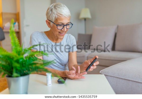 Happy mature woman with glucometer\
checking blood sugar level at home. Woman testing for high blood\
sugar. Woman holding device for measuring blood\
sugar