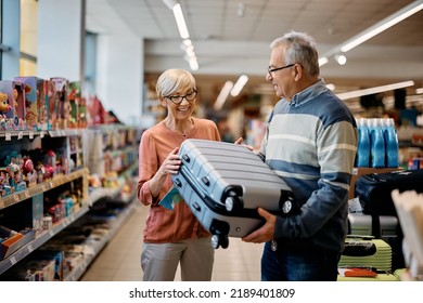 Happy Mature Woman And Her Husband Buying Travel Bag In Supermarket.