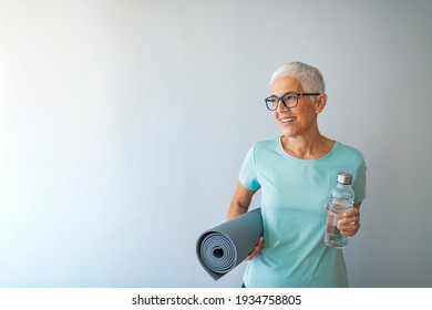 Happy Mature Woman Holding A Yoga Mat In Health Club. Fitness Female After Work Out Session In Gym. Portrait Of Mature Woman With Yoga Mat. 