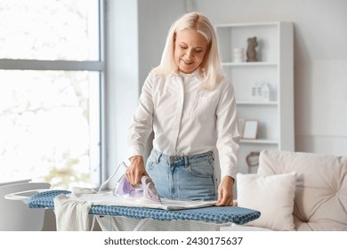 Happy mature woman ironing clothes at home - Powered by Shutterstock