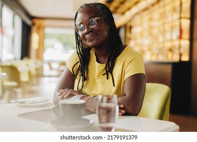 Happy mature woman looking at the camera while sitting in a cafe. Cheerful woman with dreadlocks spending some time alone in a restaurant. - Powered by Shutterstock