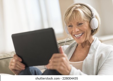 Happy Mature Woman Looking At Digital Tablet While Using Headphones At Home