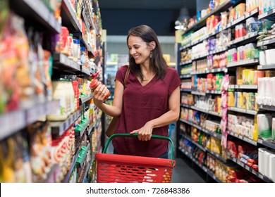 Happy mature woman looking at product at grocery store. Smiling hispanic woman shopping in supermarket and reading product information. Costumer buying food at the market. - Powered by Shutterstock