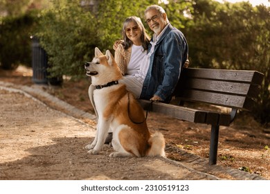 Happy mature woman and man in casual and sunglasses sit on bench with dog, enjoy walk in park outdoor. Love, relationships, free time and weekend with pet, retirement and active lifestyle - Shutterstock ID 2310519123