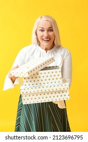 Happy Mature Woman Opening Gift Box On Yellow Background. International Women's Day Celebration