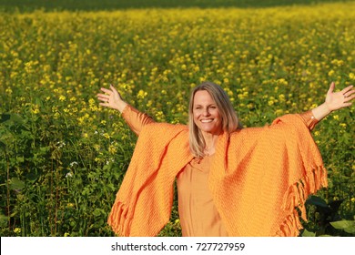 Happy Mature Woman With Orange Shawl Spread Her Arms In A Flower Field