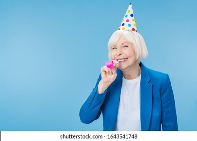 Happy Mature Woman In Party Hat Making Noise Isolated On Blue Background