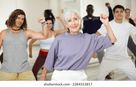 Happy mature woman practising modern dance moves with other people in dance studio - Powered by Shutterstock