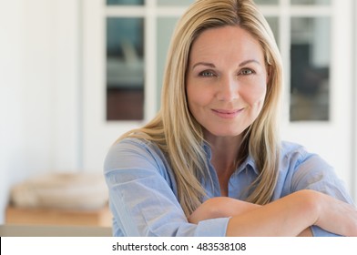 Happy Mature Woman Relaxing On Her Couch At Home In The Living Room. Close Up Face Of Senior Woman Looking At Camera. Portrait Of Happy Woman In Blue Shirt Smiling.