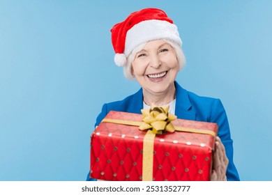 Happy mature woman in Santa hat holding red gift box isolated over blue background. Happy holiday! Happy New Year Eve celebration! Merry Christmas! - Powered by Shutterstock