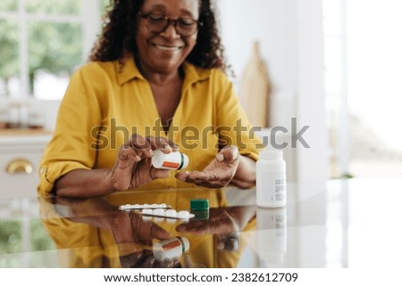 Happy mature woman sitting at her kitchen table and taking daily medication to manage a chronic condition. Woman adhering to her prescribed treatment plan to maintain her health and quality of life.