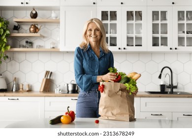 Happy Mature Woman Unpacking Paper Bag With Fresh Organic Vegetables In Kitchen After Grocery Shopping Or Delivery, Happy Lady Enjoying Healthy Nutrition, Standing Near Table And Smiling At Camera - Powered by Shutterstock