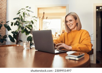 Happy mature woman using laptop while working remotely from home in living room